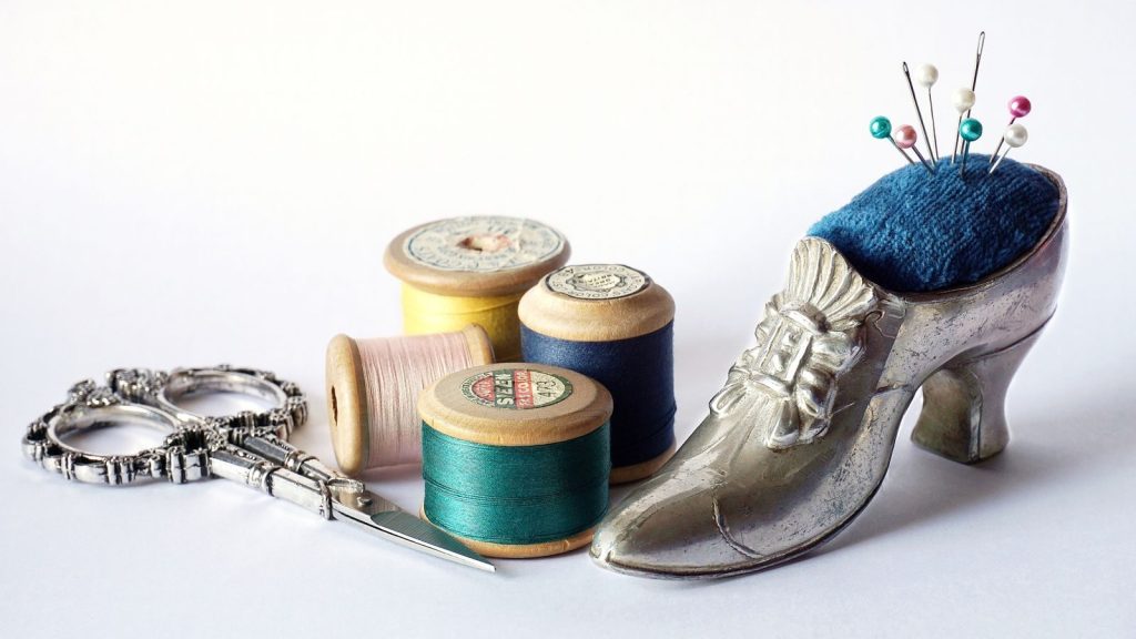 Elegant display of vintage sewing tools including scissors, thread spools, and a shoe-shaped pincushion.