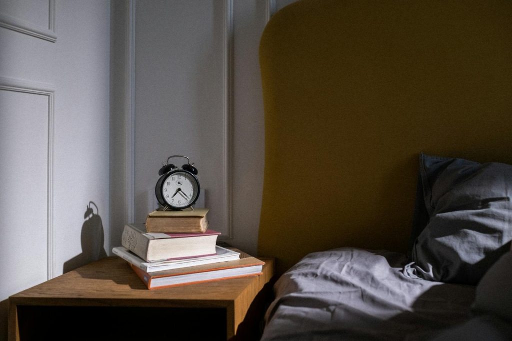 A cozy bedroom setting with books and an alarm clock on a nightstand next to a bed.