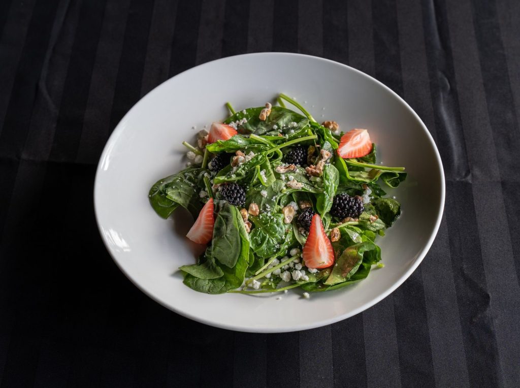 A close-up of a fresh spinach salad with strawberries, walnuts, and blackberries on a white plate.