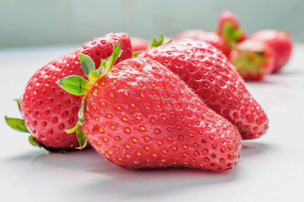 Close-up of ripe, fresh strawberries on a white surface showing vibrant red color and green leaves.