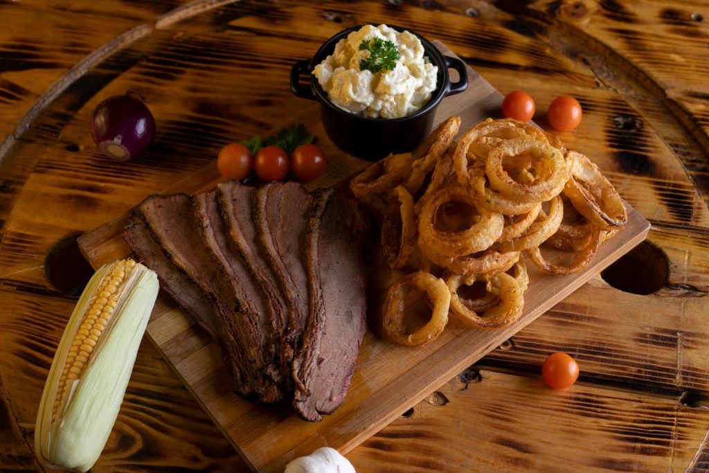 Delicious BBQ platter featuring tender steak, crispy onion rings, and fresh side dishes on a wooden board.