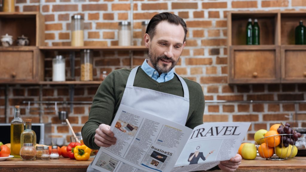 man reading travel newspaper in kitchen