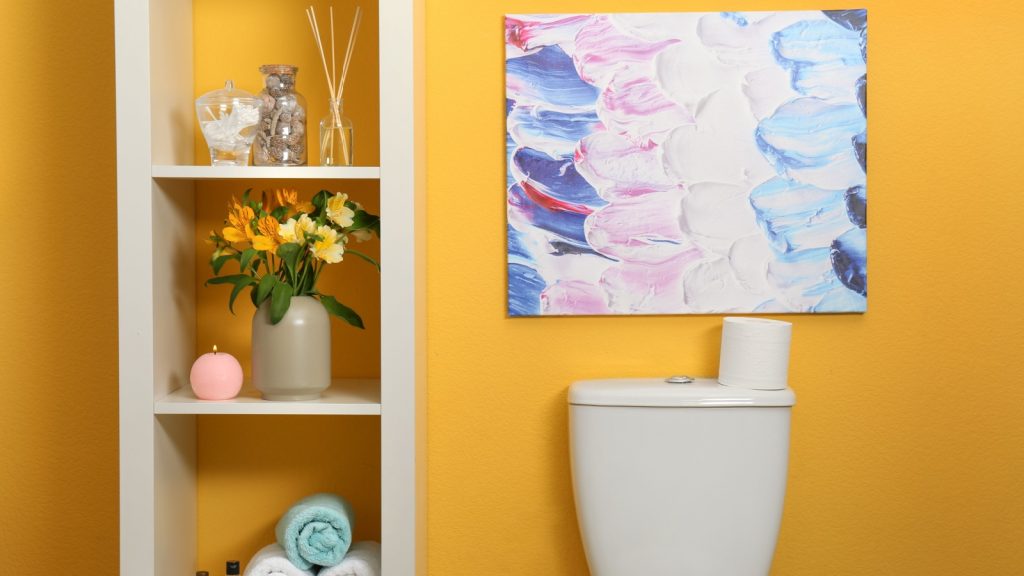 Shelves with different stuff above toilet bowl near orange wall in restroom interior