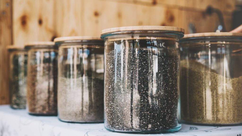 Chia, different seeds and other superfoods in glass jars on table. Organic bulk products in zero waste shop. Foods storage in kitchen at low waste lifestyle. Shopping in plastic free grocery store.