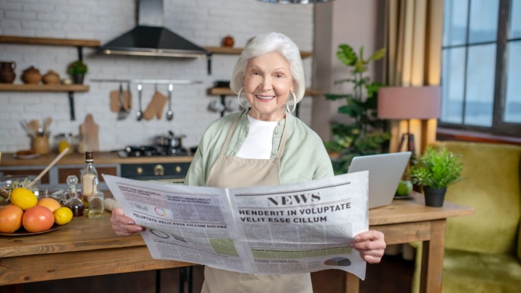 Print newspaper. A smiling elderly woman reading a big newspaper