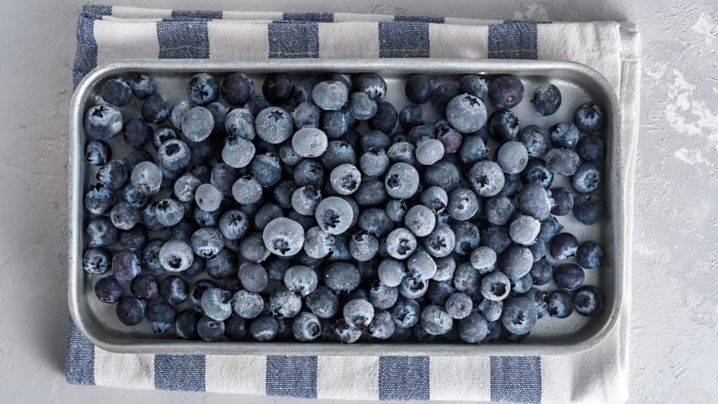 Frozen blueberries in a metal tray on a concrete background.