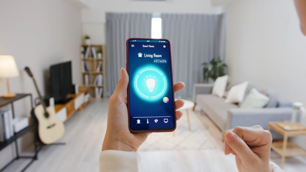 Asian young woman is using smart home app and touch screen to turn on the light by mobile phone