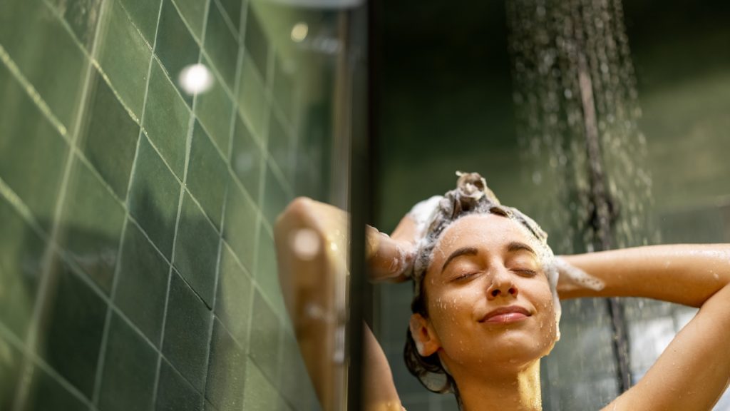 Happy woman with closed eyes in shower rinse shampoo with water dripping on face. Taking shower and relaxing under warm running water. Copy space.
