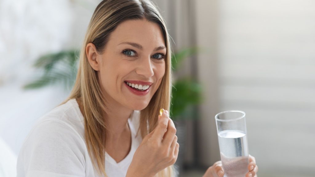 Healthy lifestyle, vitamins and minerals, supplements in diet concept. Smiling pretty young woman taking pill after waking up, holding gelatin capsule and glass of water, copy space