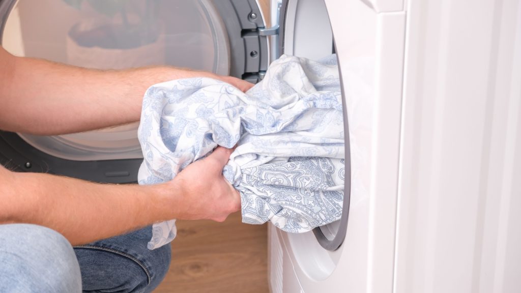 tumble dryer. A man takes dried bed linen out of the tumble dryer. Dryer machine in the house.