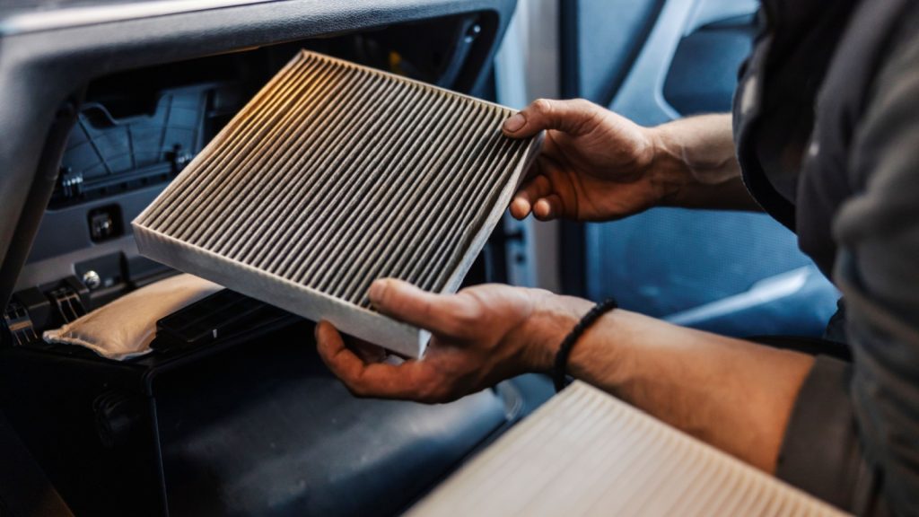 Close up of a car workshop worker taking out dirty and old air filter in car.