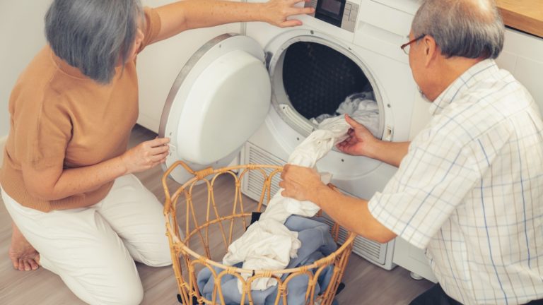 Senior couple working together to complete their household chores at the washing machine in a happy and contented manner. Husband and wife doing the usual tasks in the house.