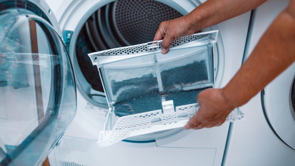 Horizontal photo of female hand taking the lint out from dirty air filter of the dyer machine 