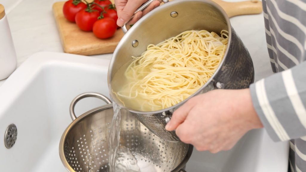Woman draining pasta into colander at sink, closeup