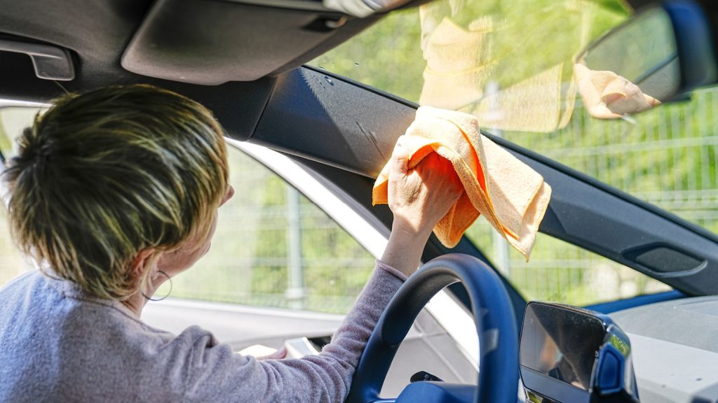 Inside view of a woman carefully cleaning the windshield on a sunny day