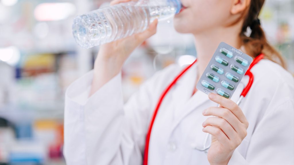 Doctor eating drug or vitamin supplements for medication and healthy with drinking clean water bottle.