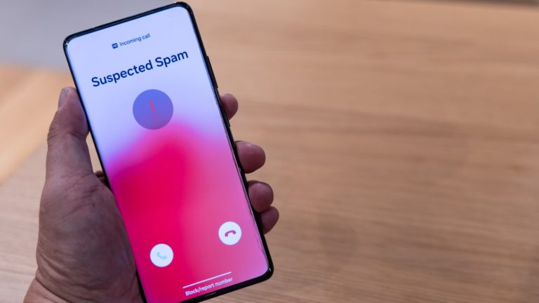 Hand holding smart phone with suspected spam incoming call warning.