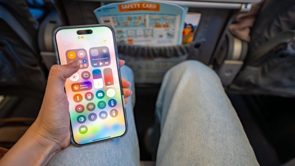 Prague, Czech republic - May 7, 2025: Woman activating airplane mode on iPhone while seated on plane before takeoff. Digital disconnection and travel preparation routine during flight. 
