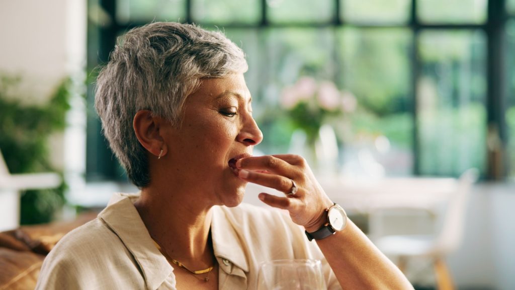 Home, healthcare and woman with pills, medicine or supplements with vitamin D, wellness and calcium. Retirement, routine and senior person with treatment in living room or prescription antibiotics