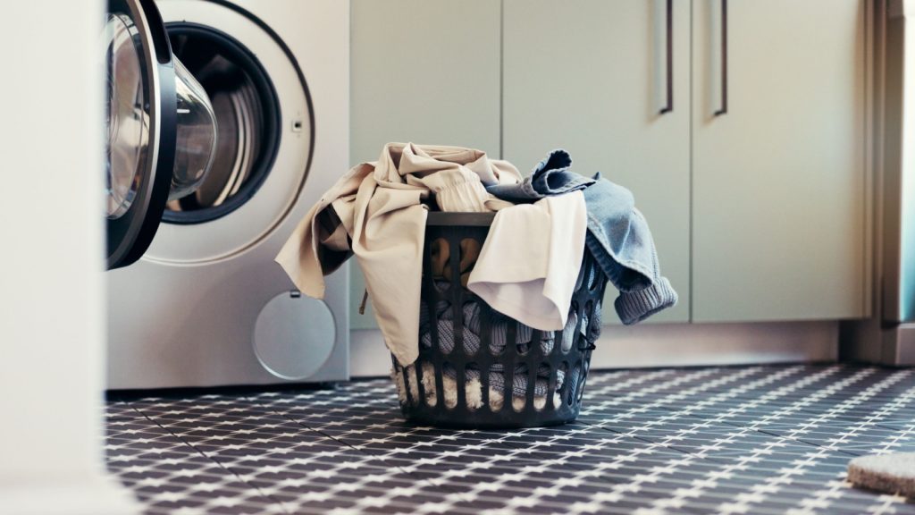 Laundry, washing machine and clothes in basket in home for housekeeping, fresh linen and hygiene. Empty, apartment and appliance with clean fabric for domestic chores, sanitation or housework routine