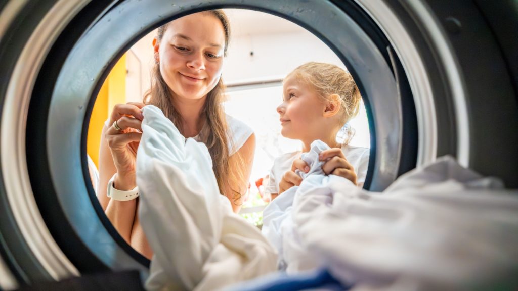 Mother and daughter doing laundry together in a self-service public laundromat, sharing household chores, building responsibility and cooperation in everyday family routine. High quality photo