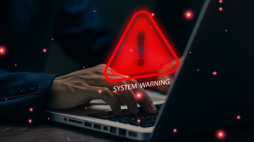 A cybersecurity warning alert appears on a laptop as a user types, symbolizing system errors, data breaches, online threats, malware risks, and digital protection in modern computer environments.