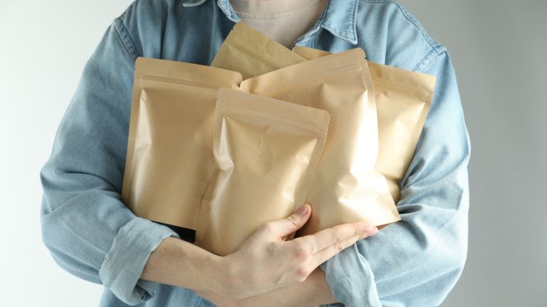 Woman with stand-up pouches on light grey background, closeup