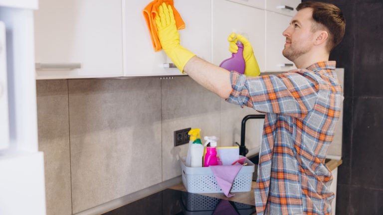 Housekeeper wearing gloves spraying detergent and cleaning kitchen cabinets with microfiber cloth