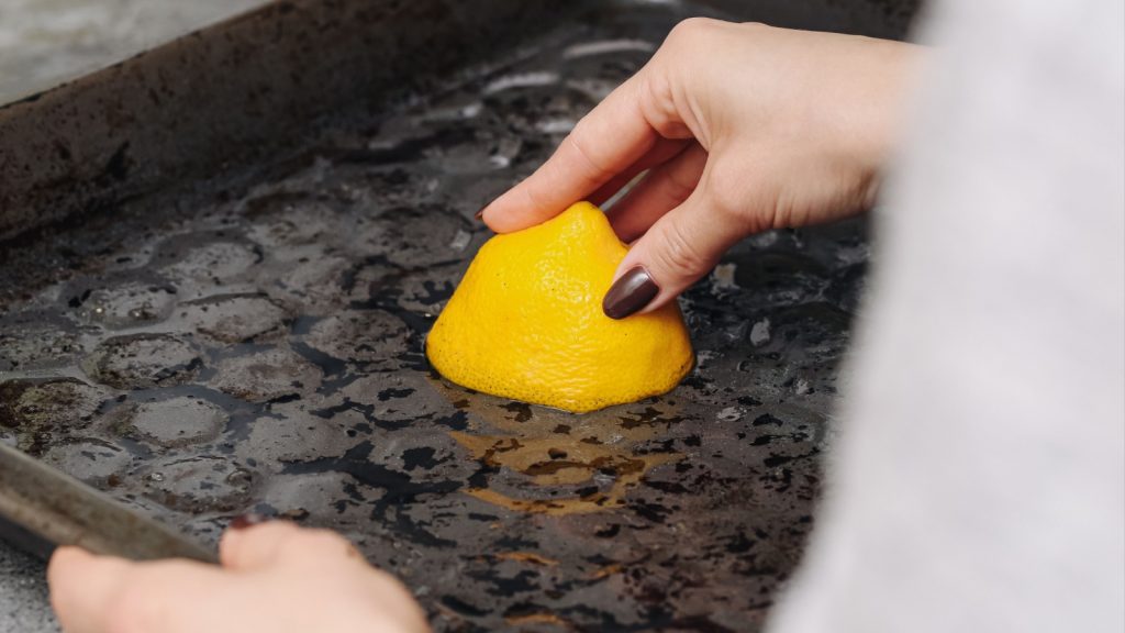 Cleaning burnt baking tray with sponge. Removing grease and stains from oven pan. Kitchen hygiene and household chores. Scrubbing dirty surface with detergent and water.