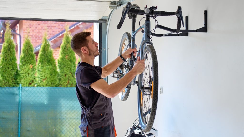 Man removes bicycle from wall rack inside garage for maintenance. Concept of home bicycle care, storage and seasonal service preparation