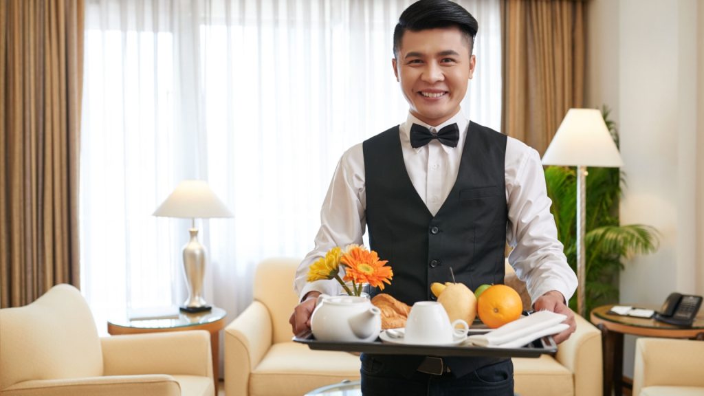 Smiling Vietnamese waiter bringing breakfast to the hotel room