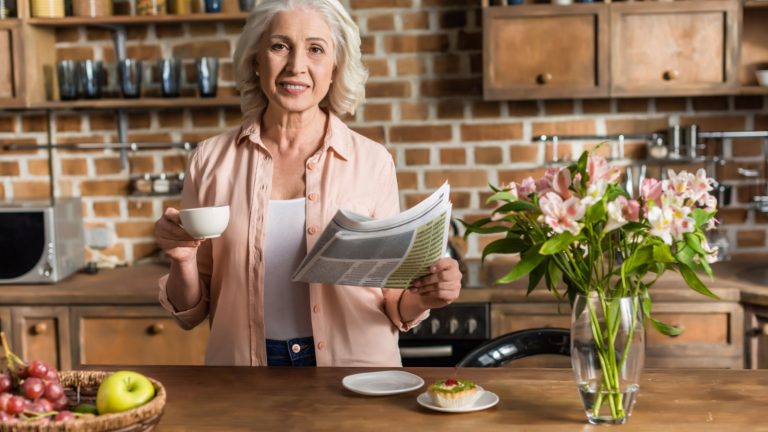 Portrait of senior woman reading newspaper during breakfast in kitchen