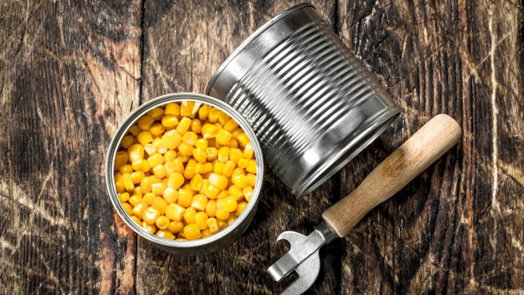 Canned corn in a tin can with opener. On a wooden background.