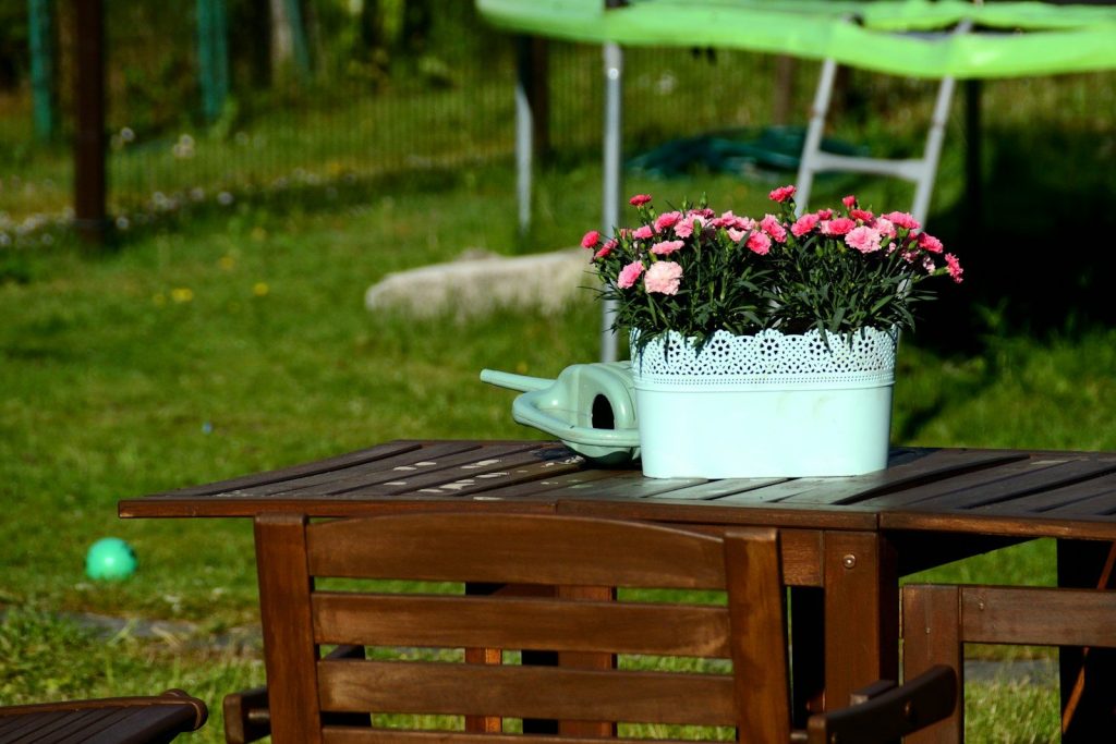 Pink flowers, watering can on wooden outdoor table.