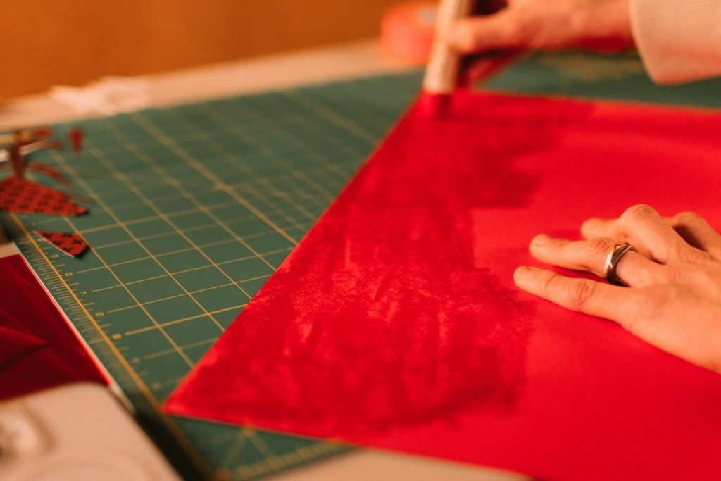Hands cutting red fabric on a green cutting mat.