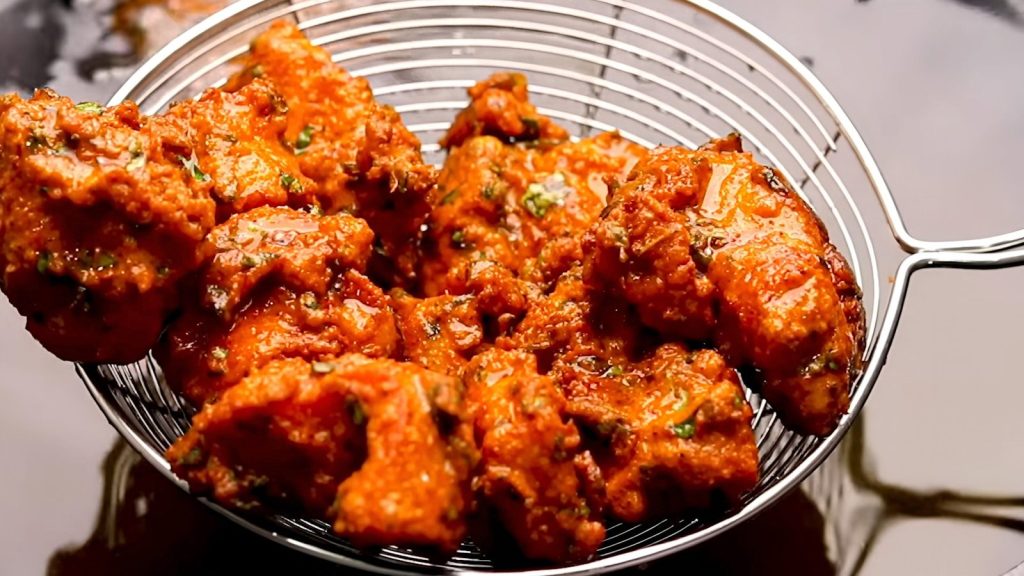 Crispy pakoras being drained in a metal strainer.