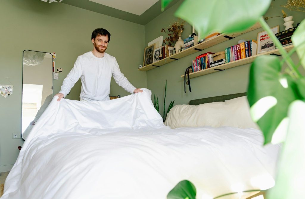 Man makes his bed in a bright, green room.