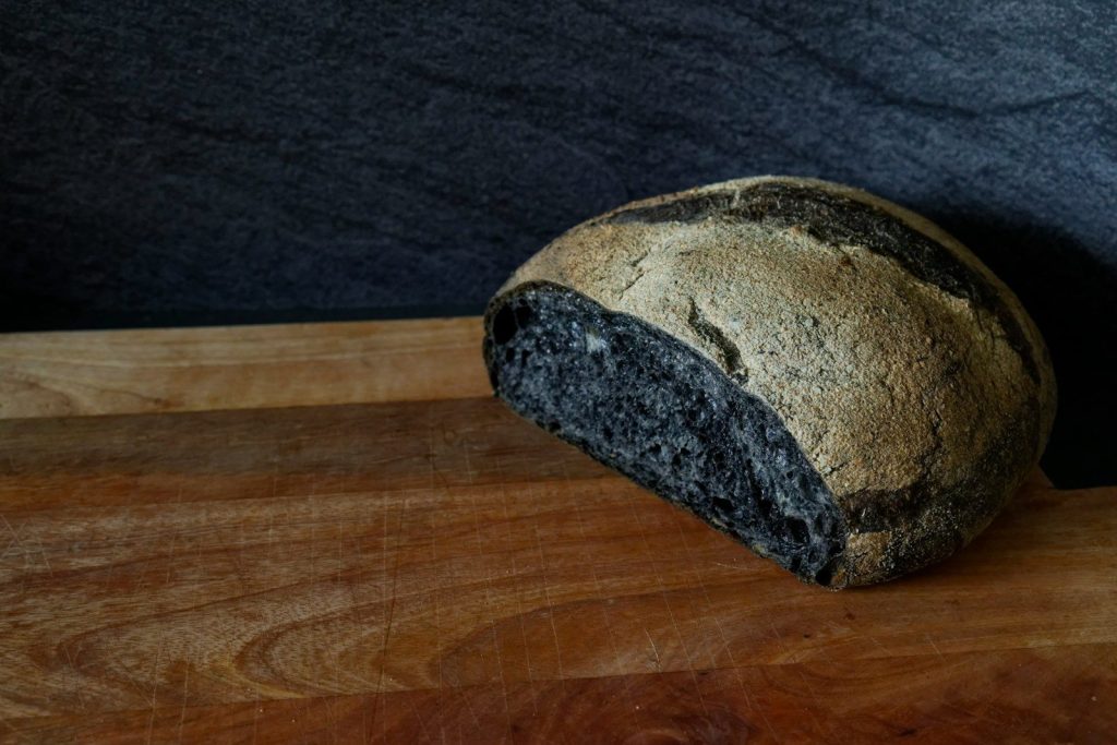 Half black, half brown bread loaf on a wooden surface.