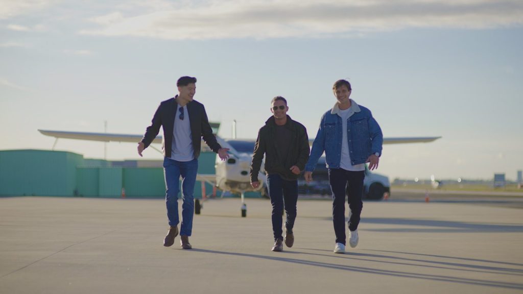Three men walking on an airfield near a small airplane.