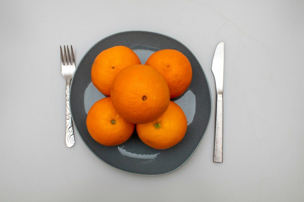 A plate of oranges on a table with a fork and knife