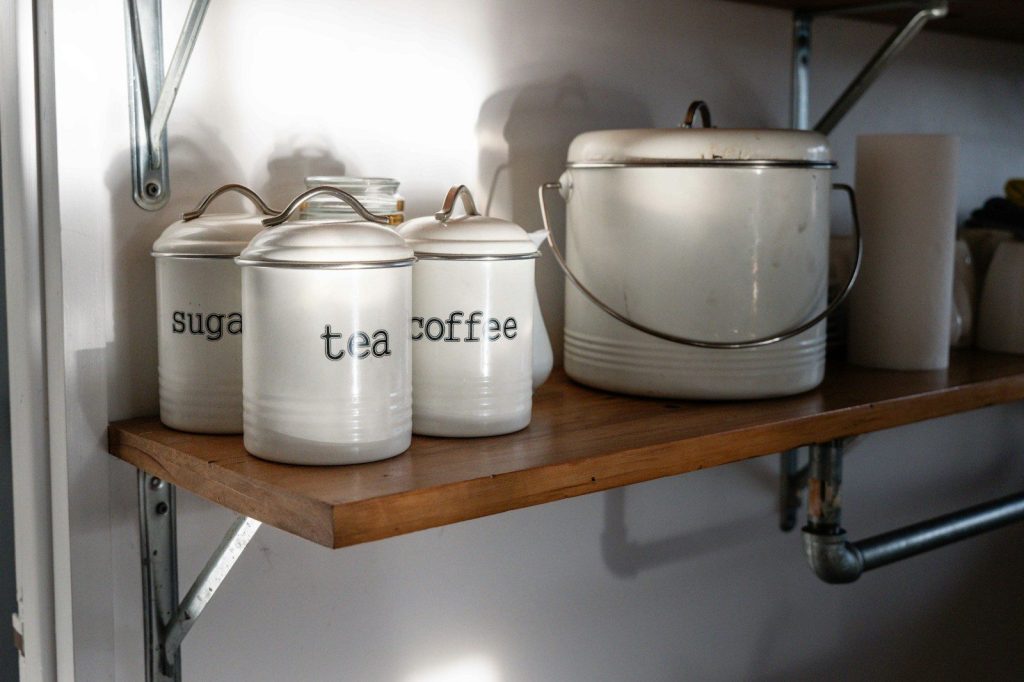 White canisters labeled sugar, tea, and coffee on shelf.
