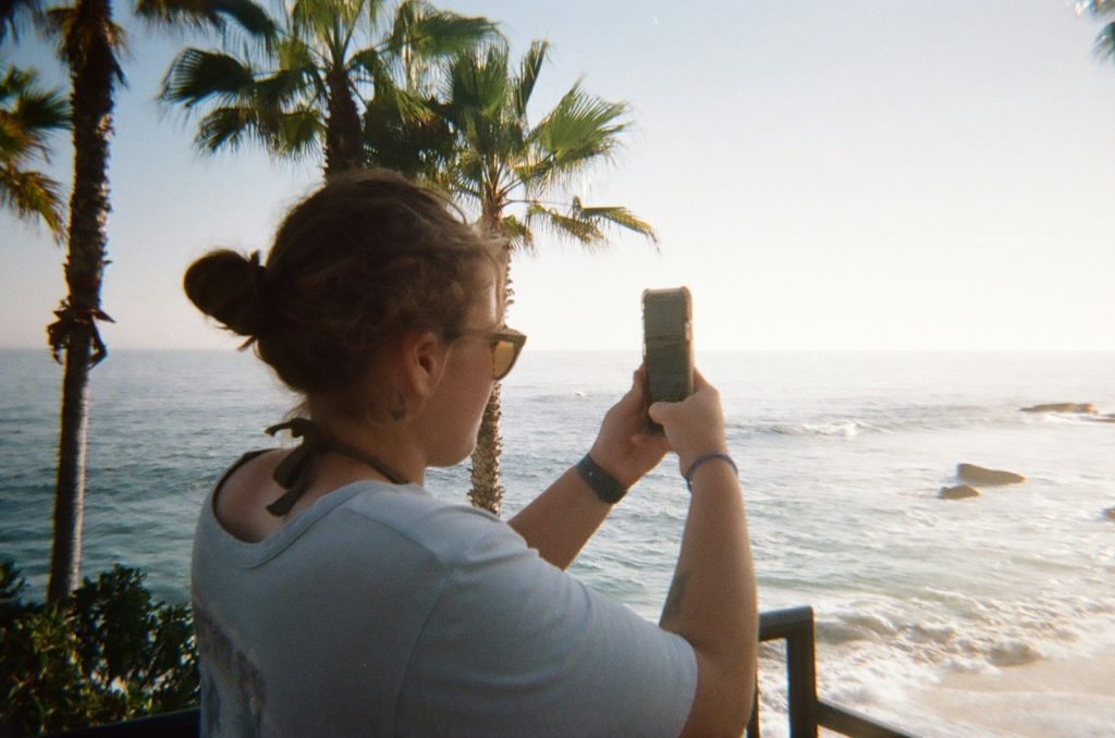 a woman taking a picture of the ocean with her cell phone