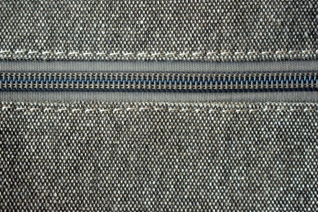 Close-up of a gray zipper on fabric with white stitching