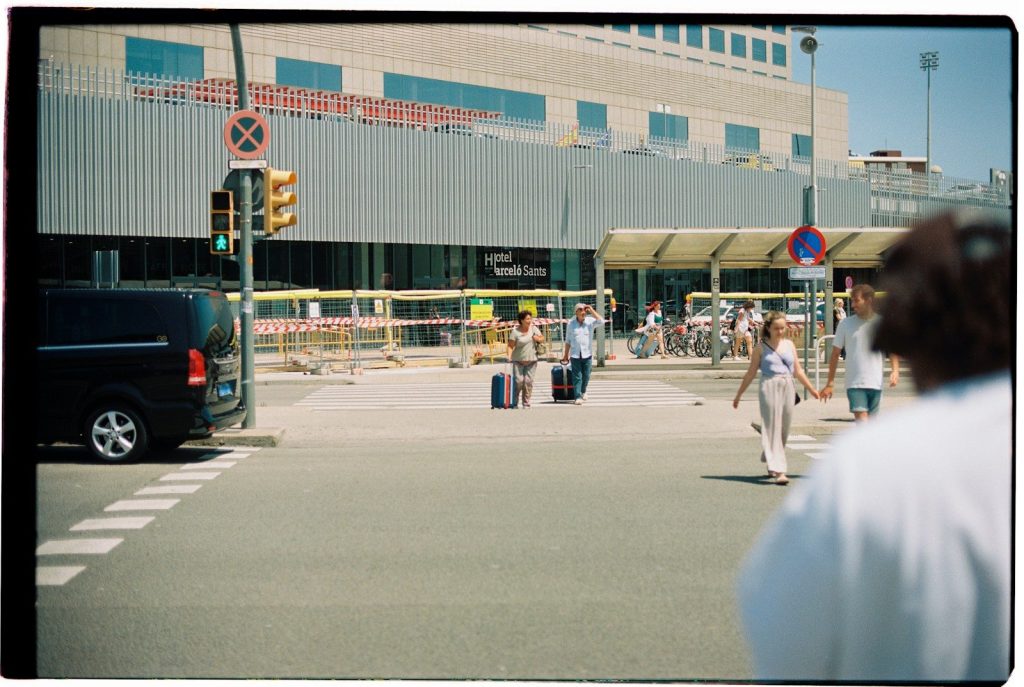 People with luggage crossing street near building.