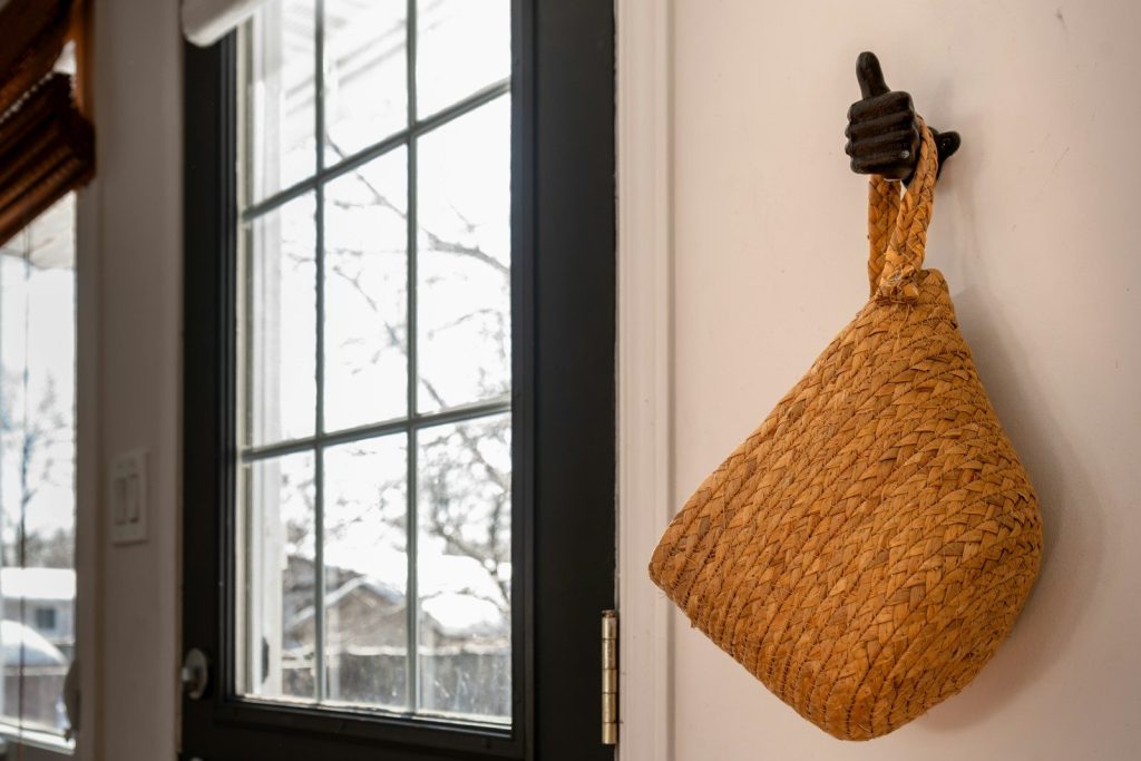 Woven basket hanging on a wall by a window.