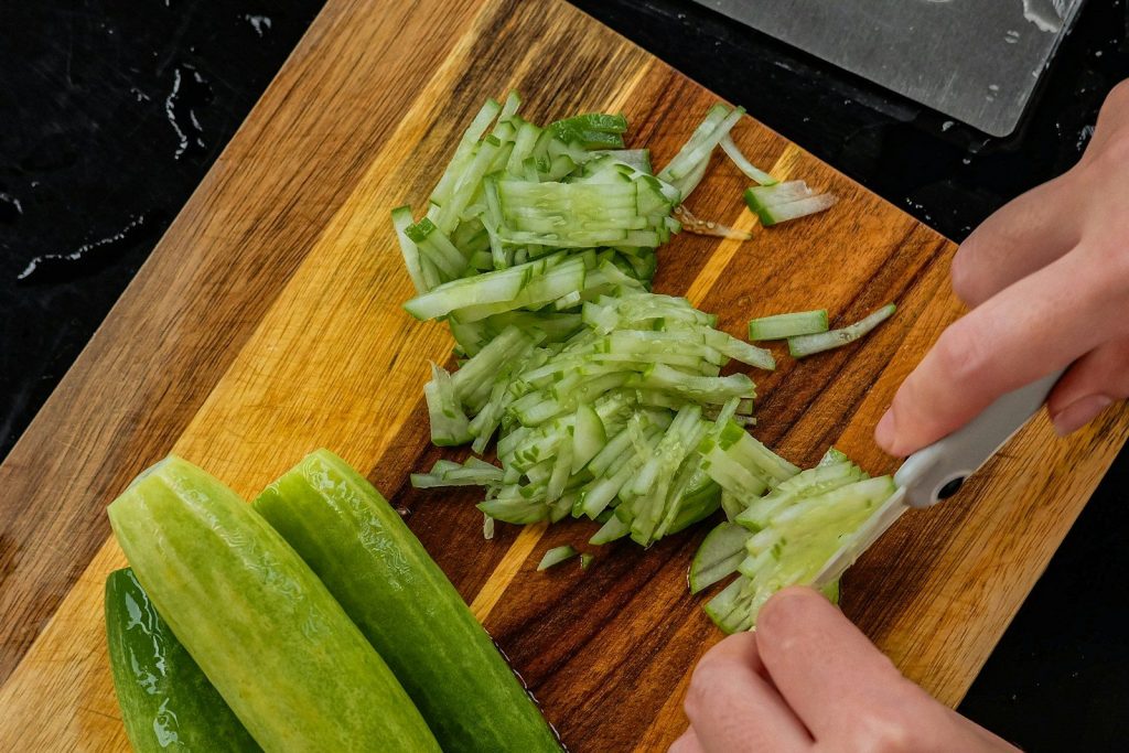 Chopping fresh cucumbers on a wooden cutting board.