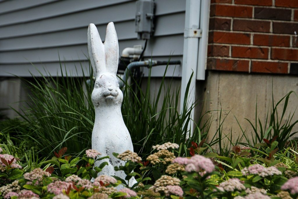 A white rabbit garden statue amongst pink flowers.