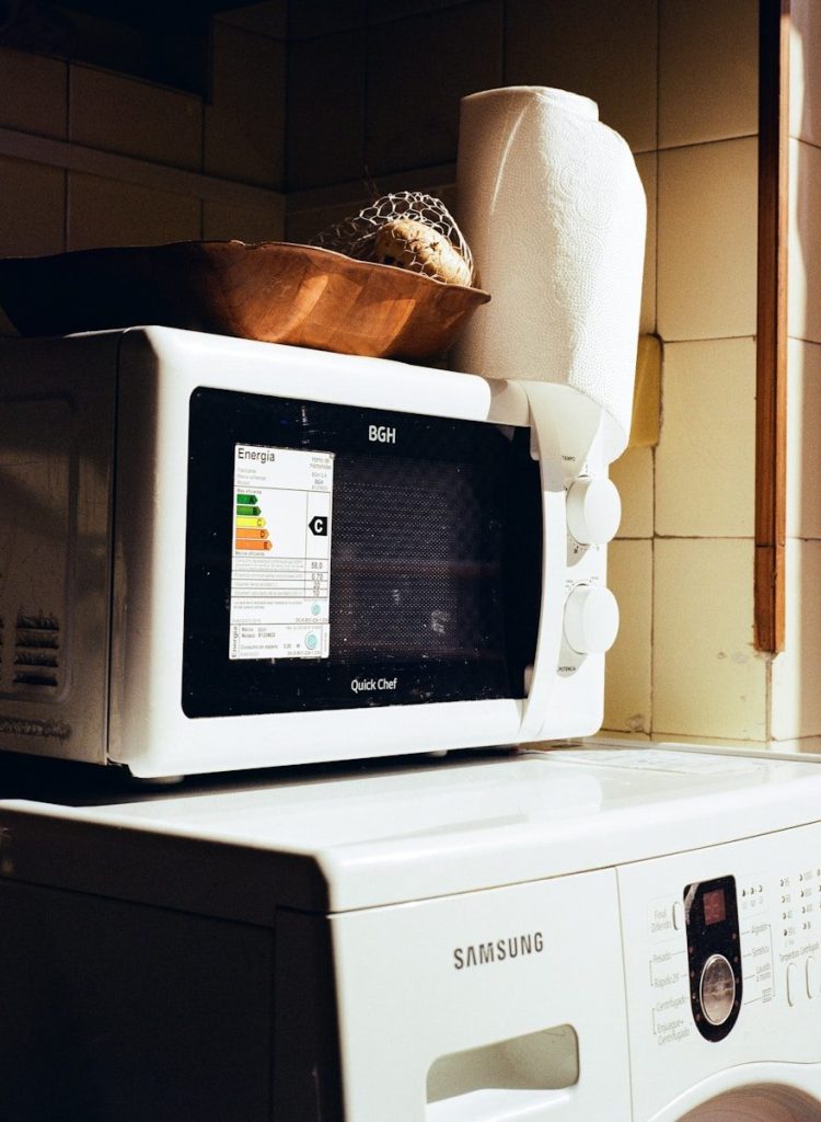Microwave oven stacked on top of a washing machine.
