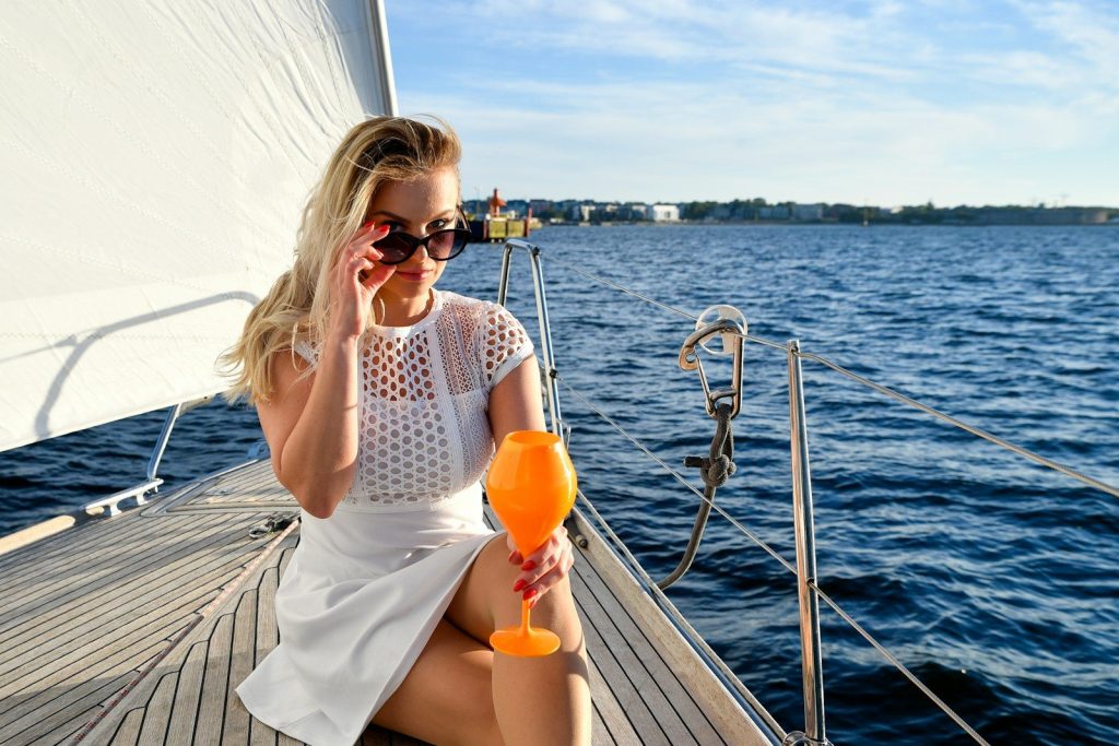 Blonde woman in sunglasses enjoying a drink on a sailboat.
