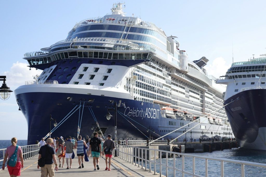 Large celebrity ascent cruise ship docked with people on pier.